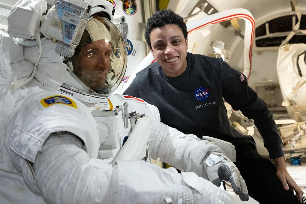 Astronauts Joshua Kutryk, in a spacesuit, and Jessica Watkins smile inside the space station's Quest airlock.
