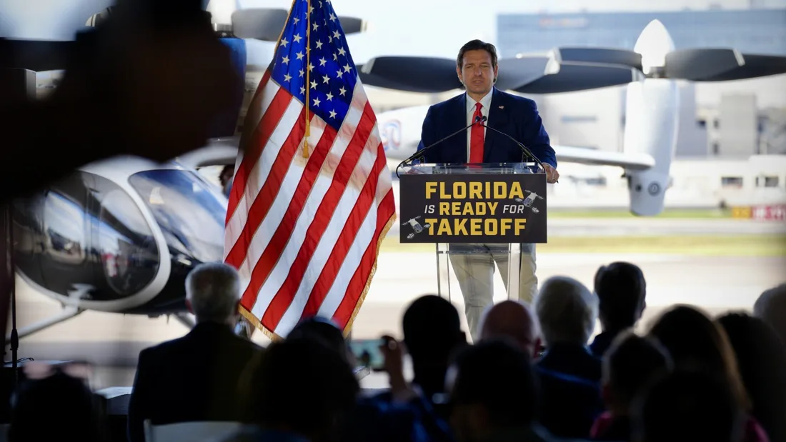 Gov. Ron DeSantis speaks at a podium reading "Florida is Ready for Takeoff" in front of an electric vertical takeoff and landing aircraft, Oct. 30, 2026.
