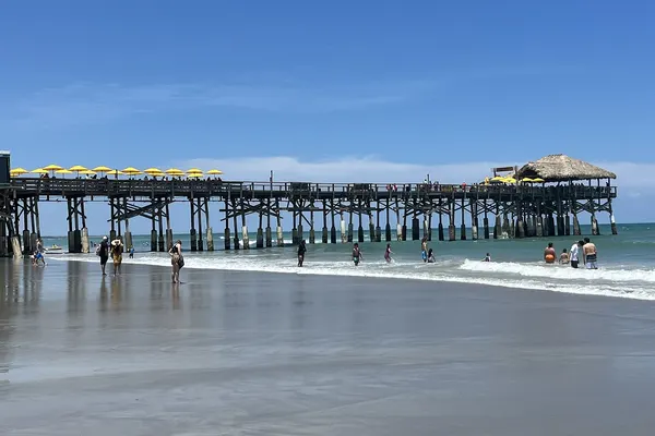 Cocoa Beach Pier stretching into the Atlantic on a sunny day, with swimmers in the shallows
