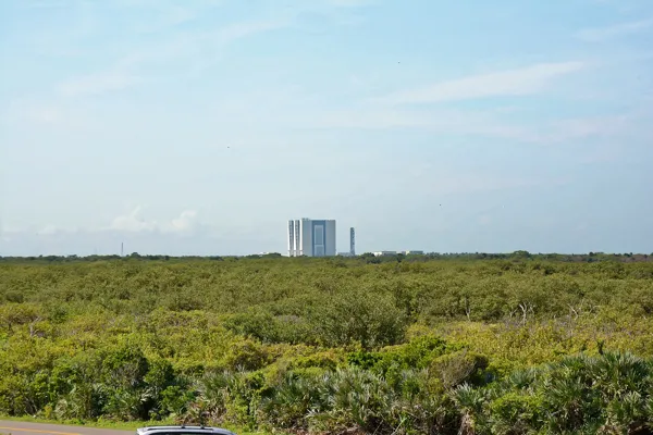 Low coastal scrub stretching to the horizon with NASA's Vehicle Assembly Building in the distance, seen from Playalinda Beach