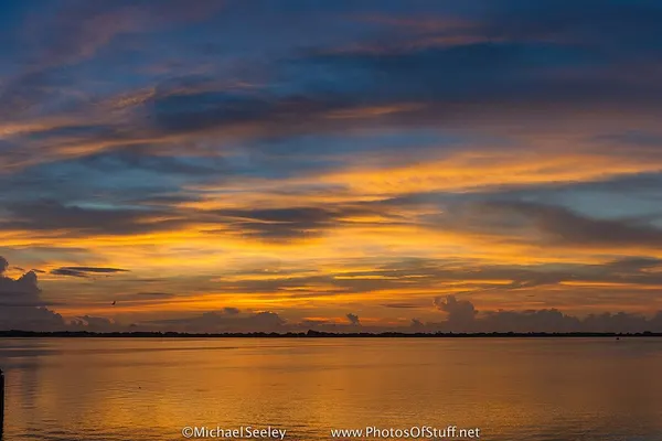 Orange and purple sky over the calm Indian River Lagoon before sunrise, with a dock silhouette